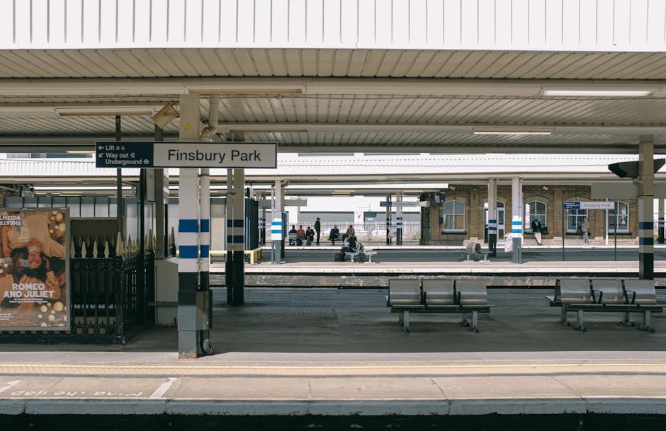 An outdoor train station with multiple railway tracks and modern yellow and grey passenger trains parked along the lines. The tracks are metal with gravel beds beneath them, running parallel and sligh